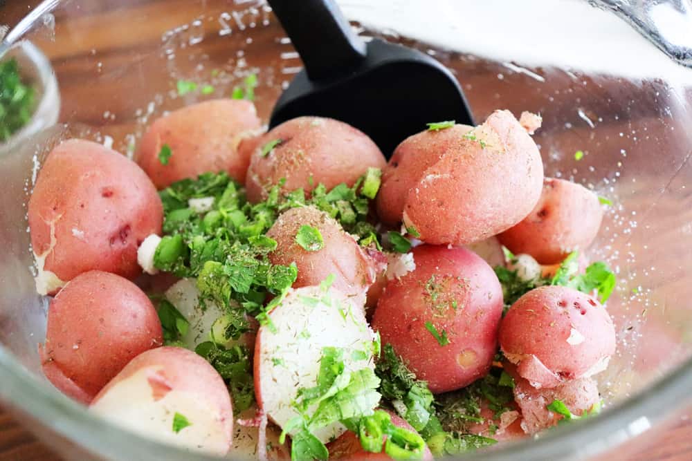 Adding sliced potatoes and herbs to mixing bowl for Warm Potato Salad with Dijon Vinaigrette