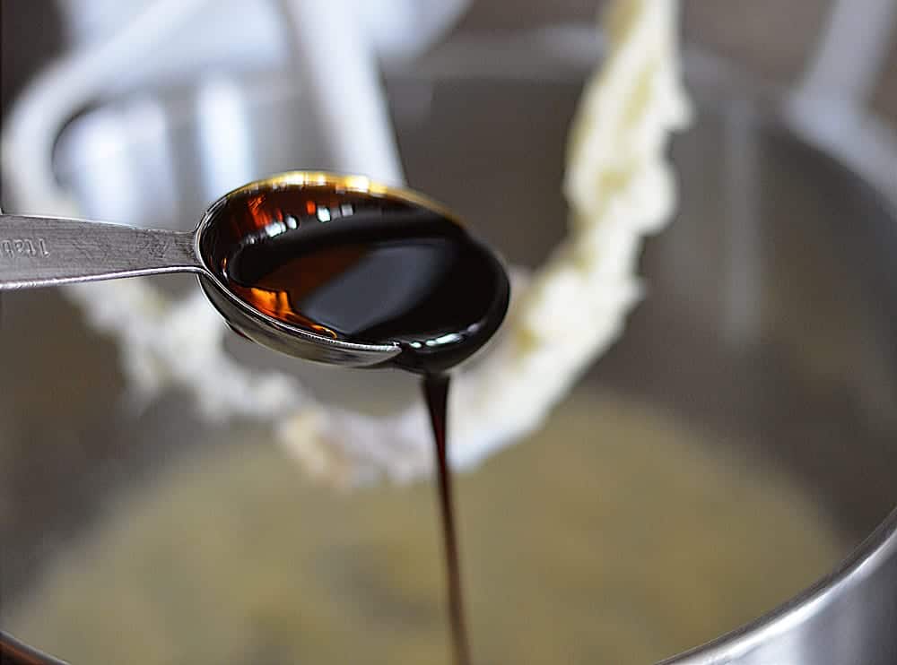 Tablespoon full of molasses drizzling into batter for Big & Chewy Vegan Oatmeal Raisin Cookies