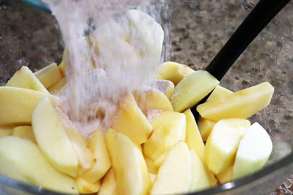 Adding cinnamon sugar to sliced apples