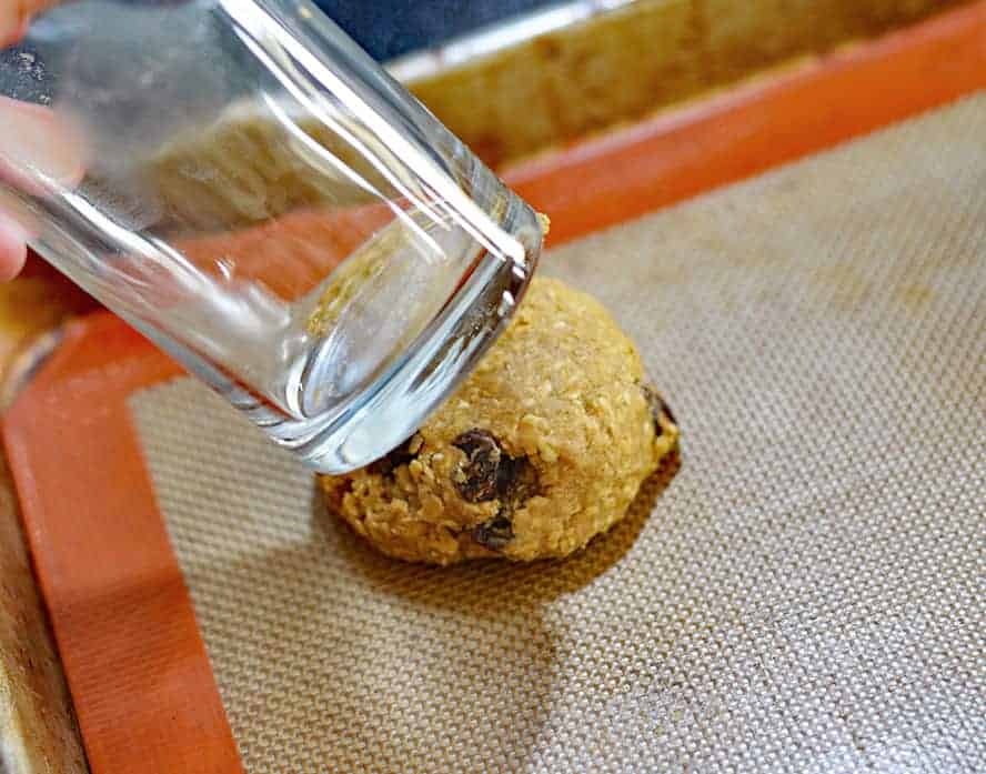 Using a glass to flatten dough for Big & Chewy Vegan Oatmeal Raisin Cookies
