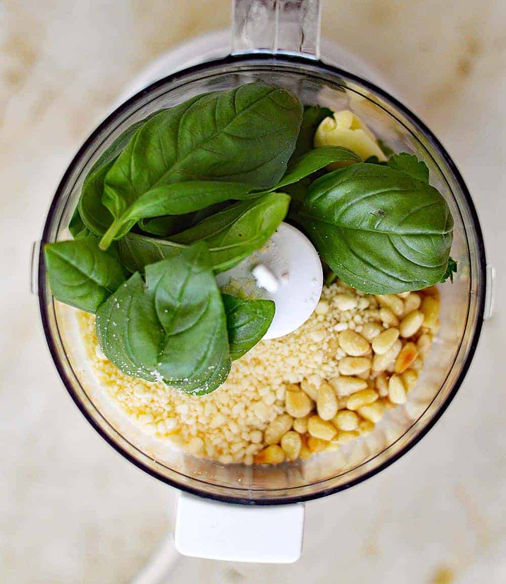 food processor filled with ingredients for basil pesto
