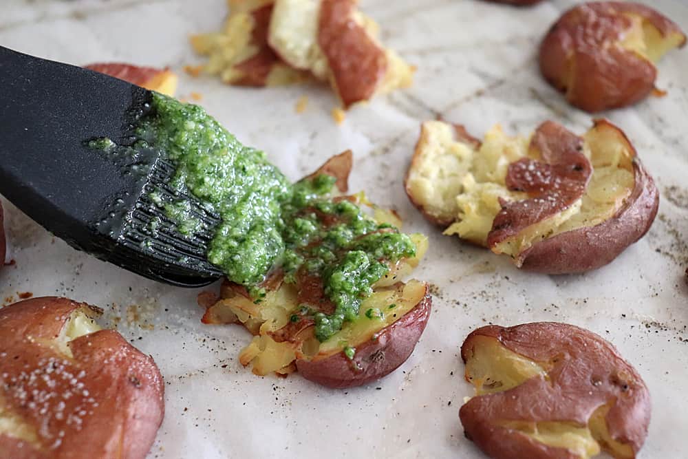 Brushing pesto on Crispy Smashed Potatoes with Parsley Pesto