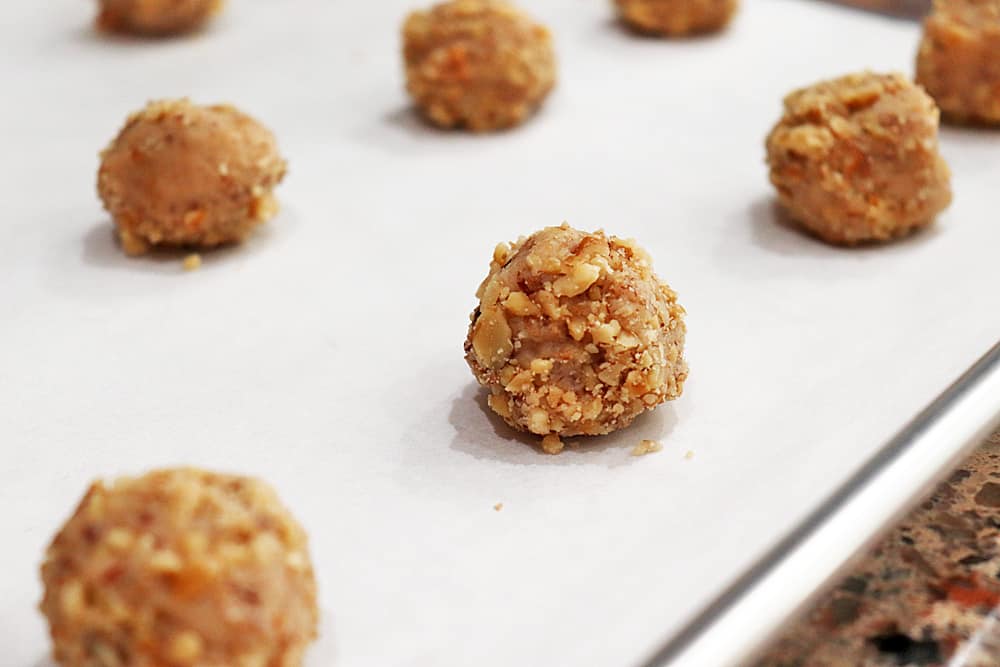 Balls of dough rolled in chopped walnuts on a cookie sheet