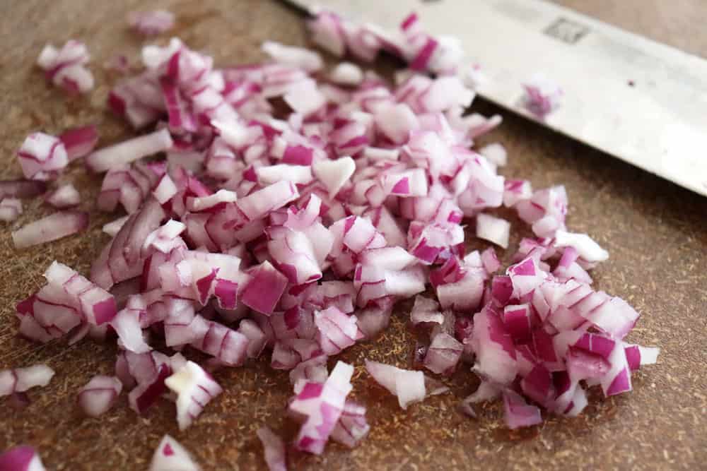 Diced red onion on a brown cutting board with a knife