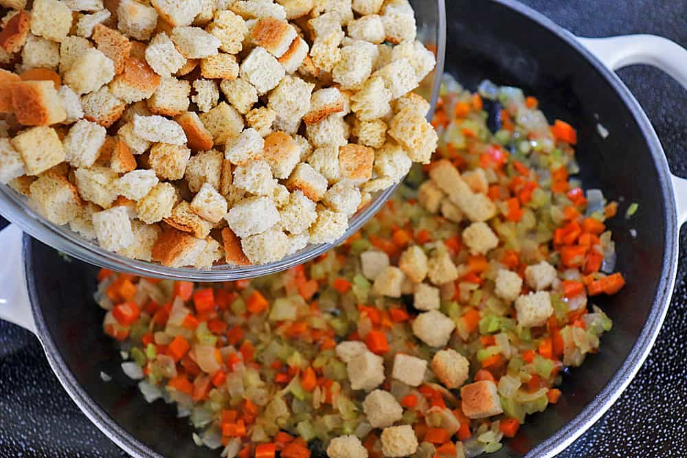 Adding dried bread cubes to the sauteed vegetables in a skillet