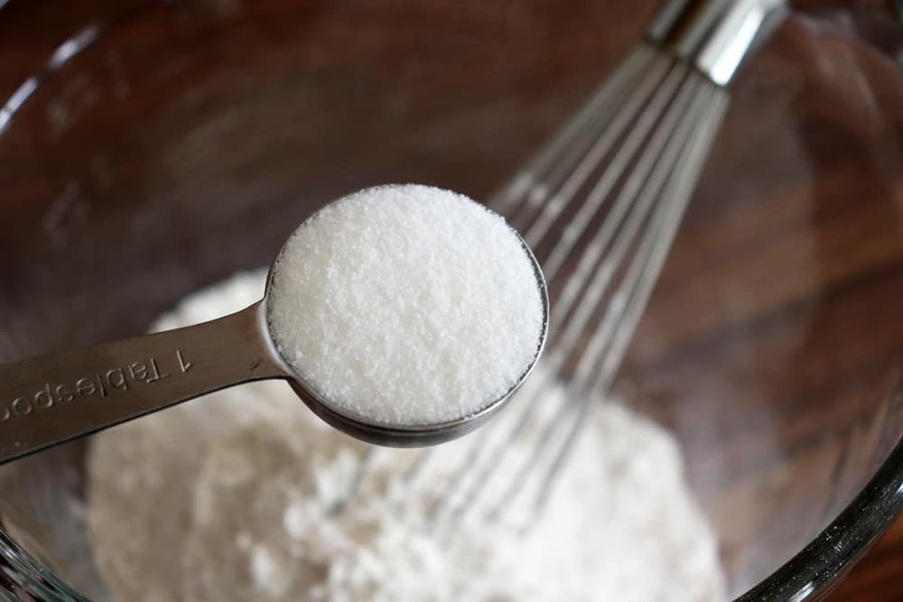 Adding sugar to a glass bowl with a whisk