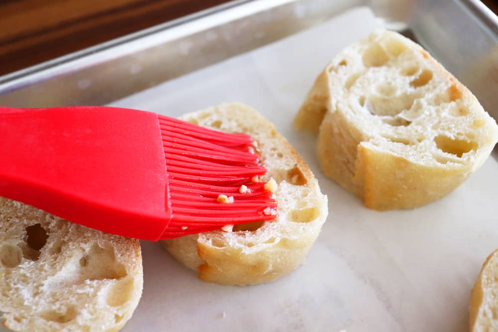 Brushing sliced baguette with olive oil garlic mixture