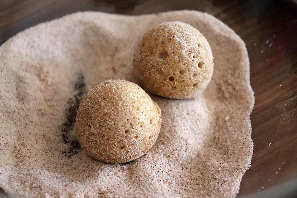 Rolling doughnuts in cinnamon sugar